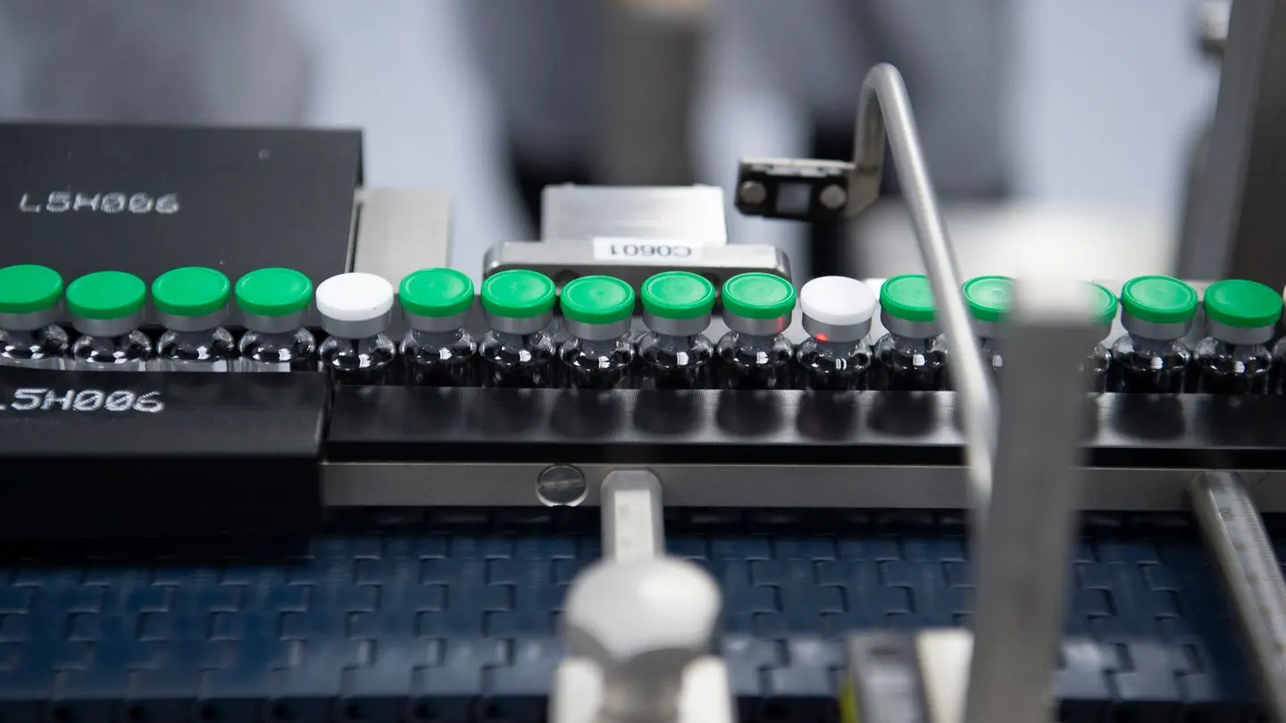 Vials with green caps moving along a pharmaceutical production line