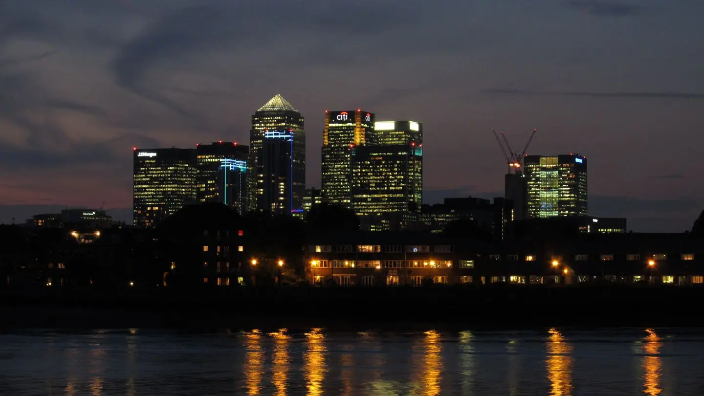 The Canary Wharf financial district skyline in London at dusk, reflected in the River Thames