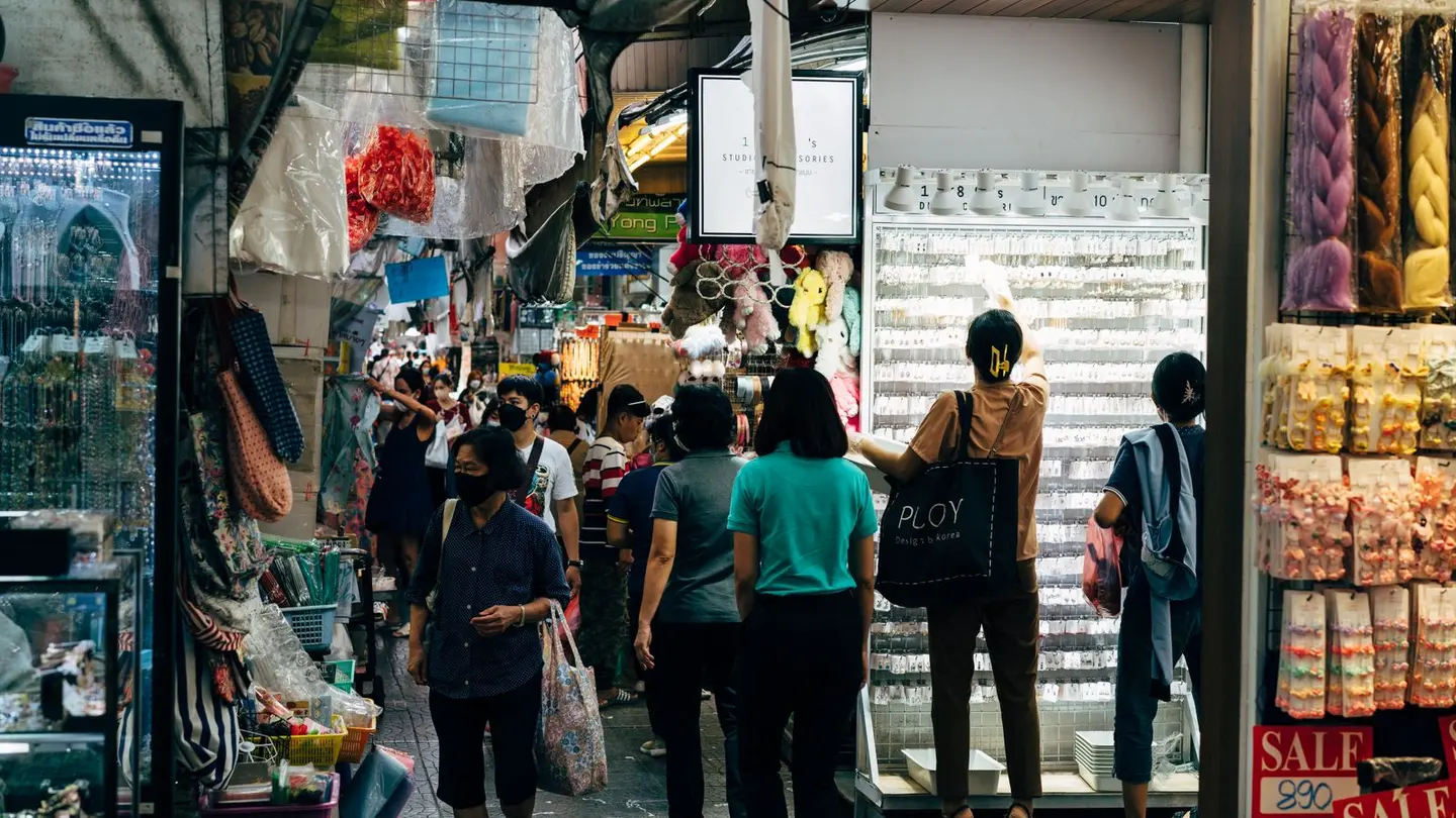 Shoppers among tightly packed stalls of a bustling market.