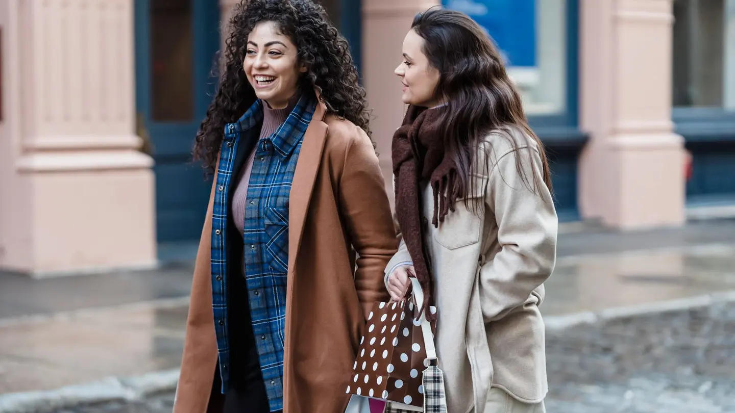 Cheerful multiethnic women walking with gift bags on street.