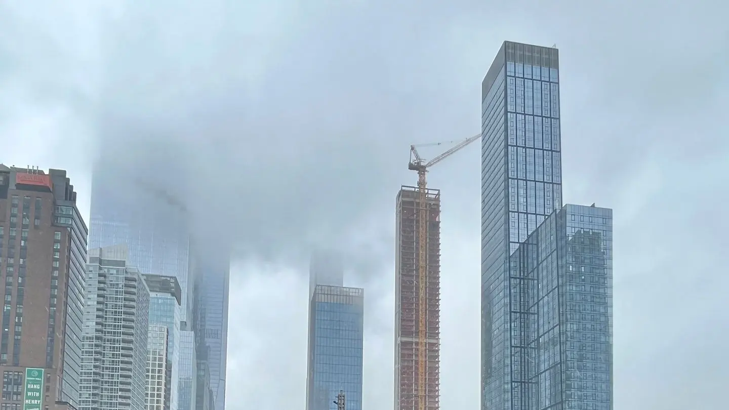 A construction crane beside new towers rising through fog near West 40th Street in New York City