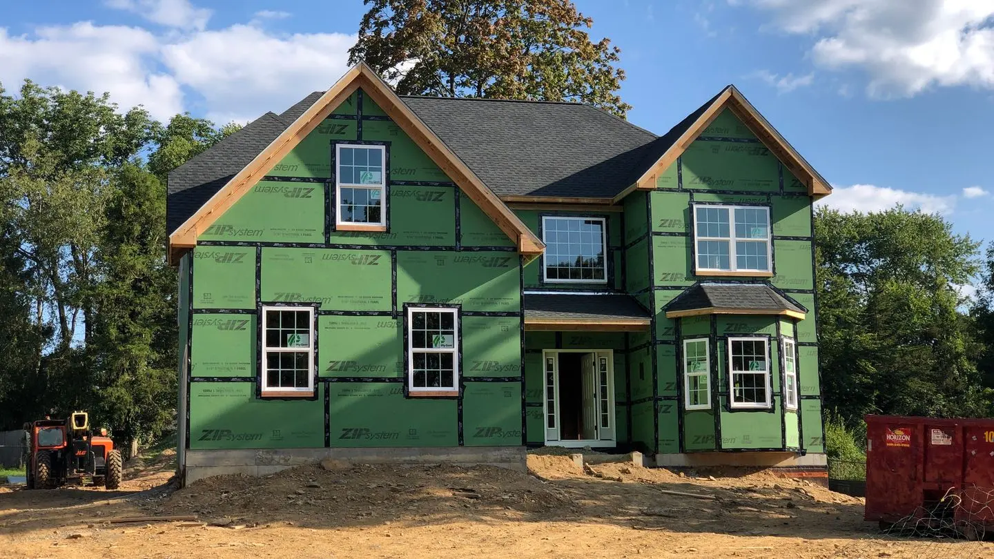 A new wood-frame house under construction in Ewing Township, New Jersey, with green sheathing and a tractor beside it